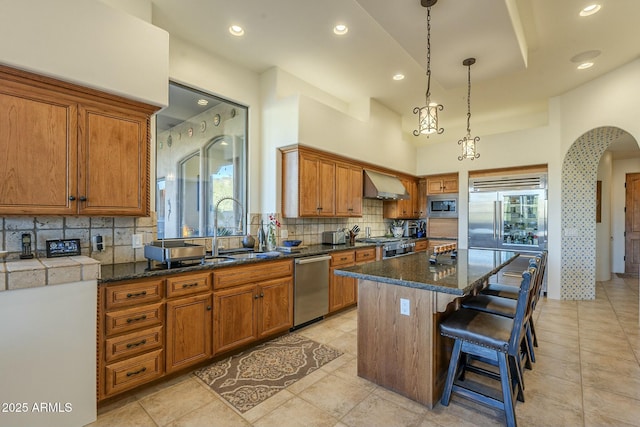 kitchen featuring sink, backsplash, built in appliances, a kitchen island, and wall chimney exhaust hood