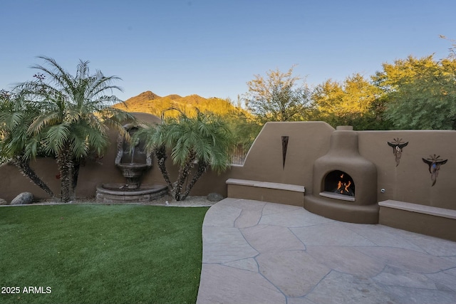 adobe home featuring an outdoor fireplace, a mountain view, a front lawn, and a patio area