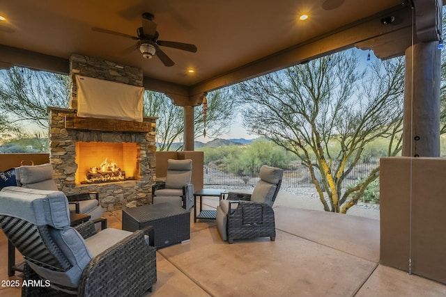 patio terrace at dusk with ceiling fan, a mountain view, and an outdoor stone fireplace