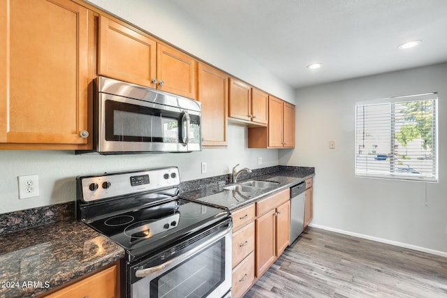 kitchen featuring light wood-type flooring, stainless steel appliances, dark stone countertops, and sink