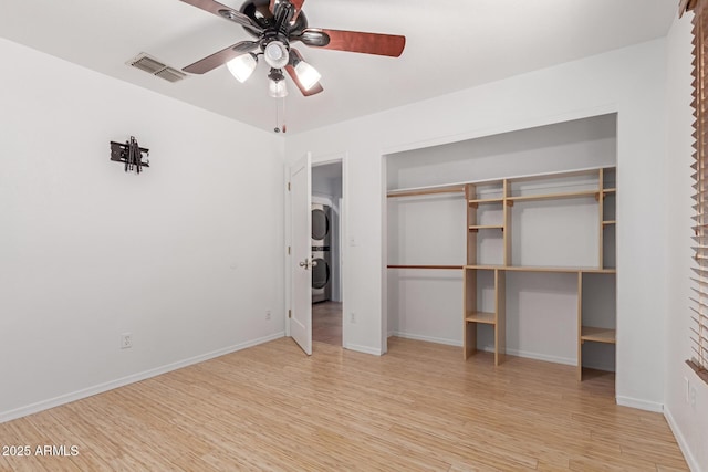 unfurnished bedroom featuring visible vents, wood finished floors, a closet, stacked washer / dryer, and baseboards