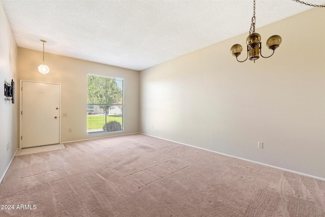 unfurnished room with light carpet, a textured ceiling, and a notable chandelier