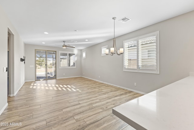 unfurnished room featuring ceiling fan with notable chandelier and plenty of natural light