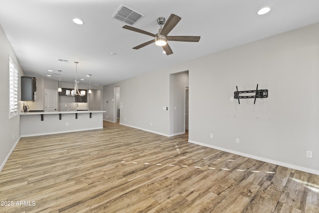 unfurnished living room with ceiling fan with notable chandelier and light hardwood / wood-style flooring