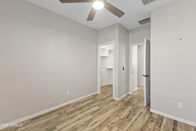 unfurnished bedroom featuring a walk in closet, light hardwood / wood-style floors, a closet, and ceiling fan