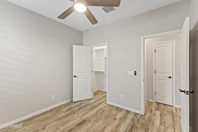 unfurnished bedroom with a walk in closet, light hardwood / wood-style flooring, a closet, and ceiling fan