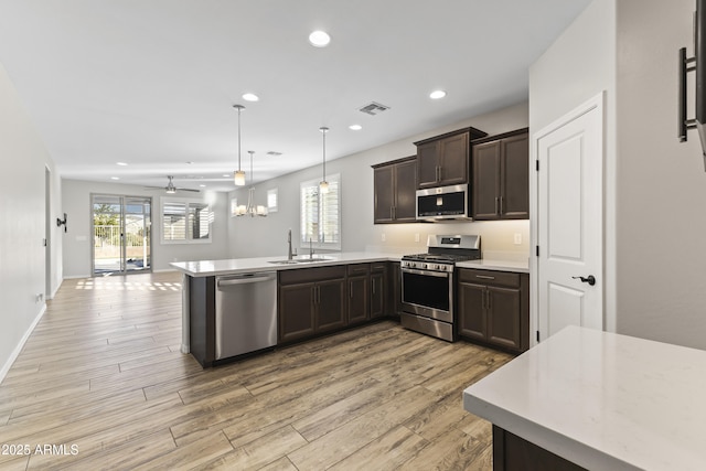 kitchen featuring decorative light fixtures, sink, kitchen peninsula, stainless steel appliances, and dark brown cabinets