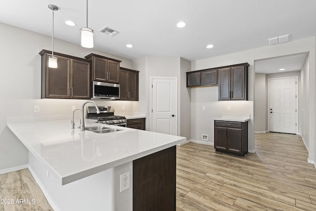 kitchen with dark brown cabinetry, light hardwood / wood-style flooring, kitchen peninsula, pendant lighting, and stainless steel appliances