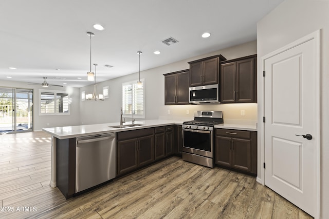 kitchen featuring sink, hardwood / wood-style flooring, hanging light fixtures, stainless steel appliances, and kitchen peninsula