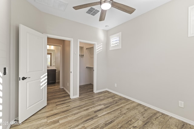 unfurnished bedroom with hardwood / wood-style flooring, a walk in closet, ceiling fan, and a closet