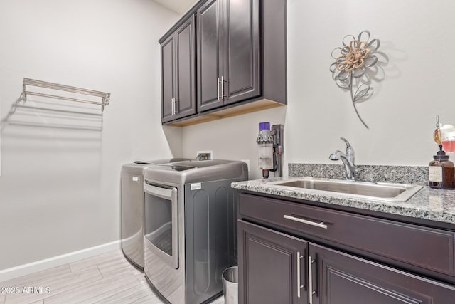 4876 N 207th Ln, Buckeye, AZ 85396 - washroom with light wood-style flooring, baseboards, a sink, cabinet space, and washing machine and clothes dryer