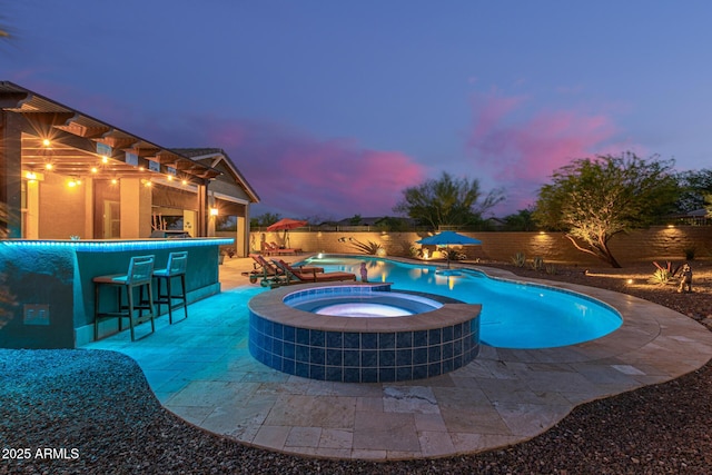 4876 N 207th Ln, Buckeye, AZ 85396 - pool at dusk featuring a patio area, a fenced backyard, a pool with connected hot tub, and outdoor dry bar