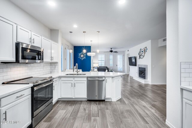 kitchen with appliances with stainless steel finishes, white cabinetry, sink, kitchen peninsula, and pendant lighting