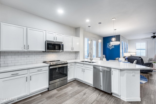 kitchen featuring white cabinetry, decorative light fixtures, kitchen peninsula, sink, and appliances with stainless steel finishes