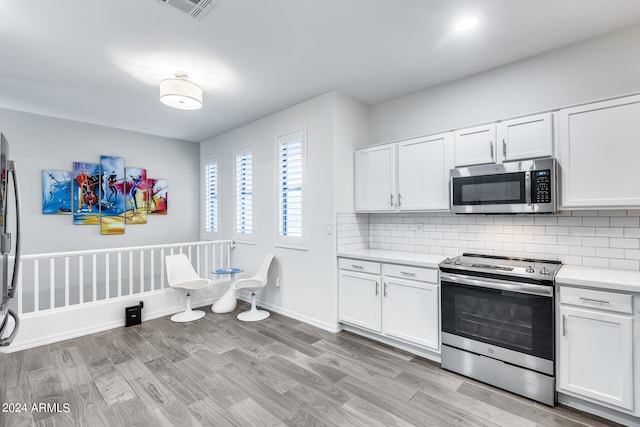 kitchen featuring appliances with stainless steel finishes, decorative backsplash, white cabinetry, and light hardwood / wood-style flooring