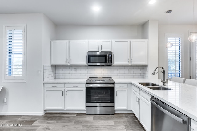 kitchen with decorative light fixtures, stainless steel appliances, white cabinetry, and sink