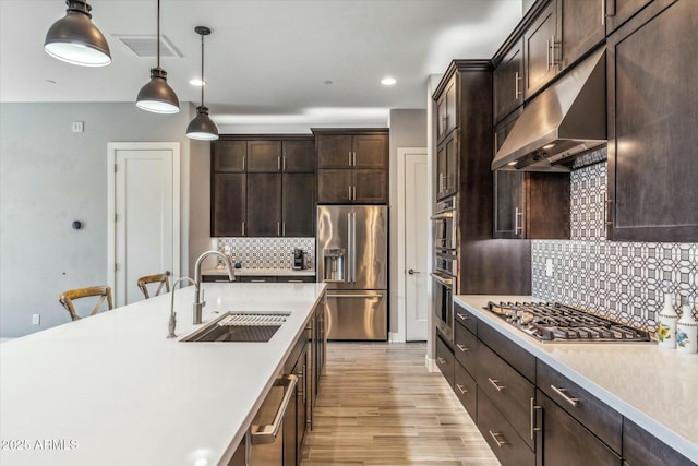 kitchen with pendant lighting, sink, appliances with stainless steel finishes, backsplash, and light hardwood / wood-style floors