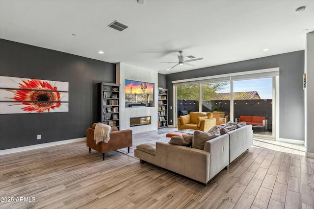 living room with ceiling fan, a tile fireplace, and light wood-type flooring