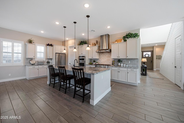 21194 W Hillcrest Blvd, Buckeye, AZ 85396 - kitchen with wall chimney exhaust hood, stainless steel appliances, a breakfast bar, light wood finished floors, and backsplash