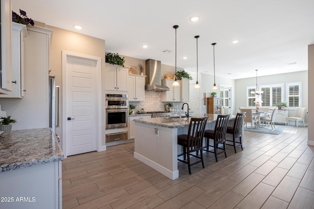 21194 W Hillcrest Blvd, Buckeye, AZ 85396 - kitchen featuring wall chimney exhaust hood, a kitchen breakfast bar, light wood finished floors, an island with sink, and backsplash