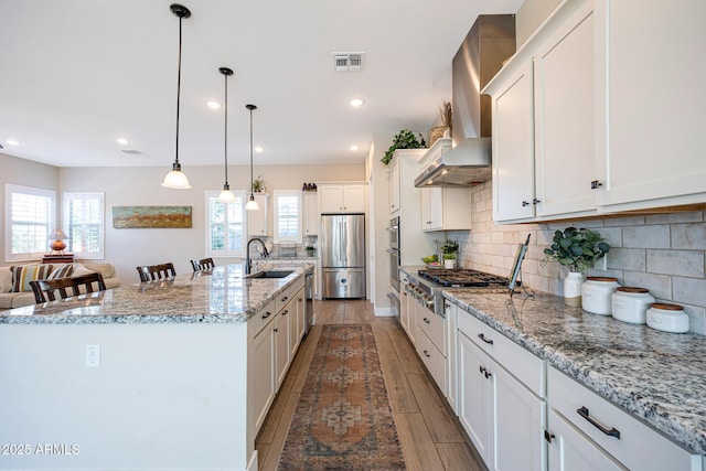 21194 W Hillcrest Blvd, Buckeye, AZ 85396 - kitchen featuring appliances with stainless steel finishes, a sink, wall chimney range hood, decorative backsplash, and white cabinetry