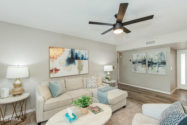 living room featuring a ceiling fan, visible vents, baseboards, and wood finished floors