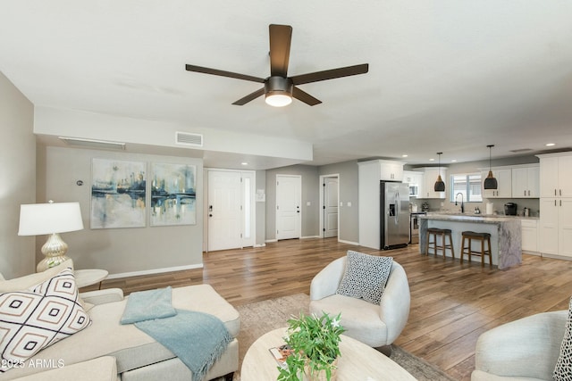 living area with a ceiling fan, visible vents, baseboards, and wood finished floors