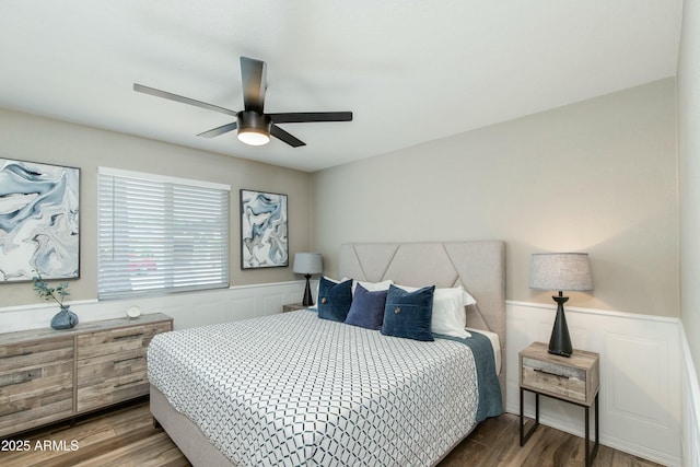 bedroom with a wainscoted wall, wood finished floors, and a ceiling fan