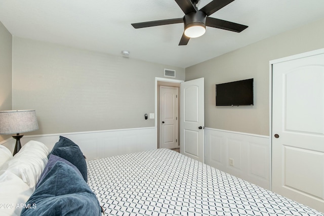 bedroom with wainscoting, visible vents, and a ceiling fan