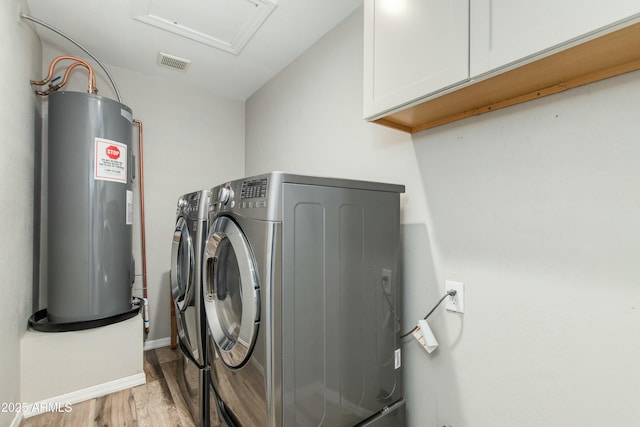 laundry area featuring washing machine and clothes dryer, cabinet space, visible vents, light wood-style flooring, and water heater