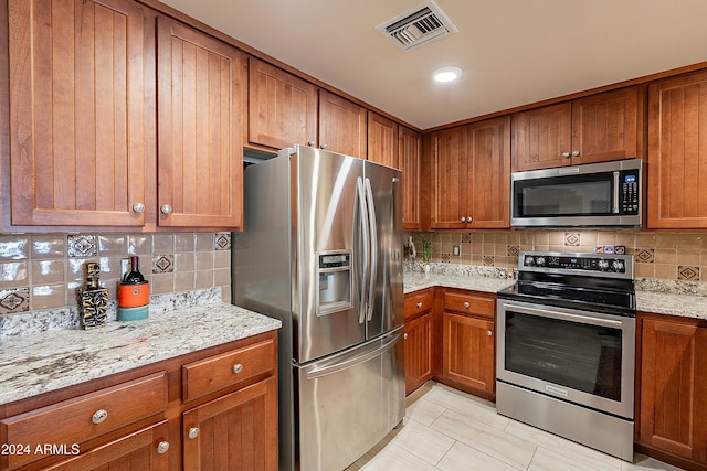 kitchen featuring light tile patterned floors, light stone countertops, backsplash, and appliances with stainless steel finishes