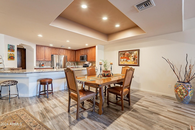 dining area featuring a tray ceiling, sink, and light wood-type flooring