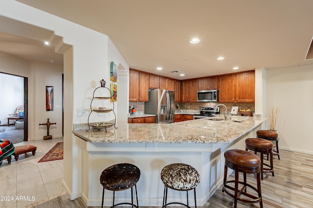 kitchen featuring a kitchen breakfast bar, light hardwood / wood-style flooring, light stone countertops, kitchen peninsula, and stainless steel appliances