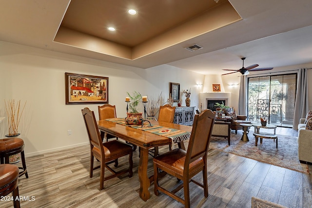 dining room featuring a raised ceiling, ceiling fan, and light hardwood / wood-style floors