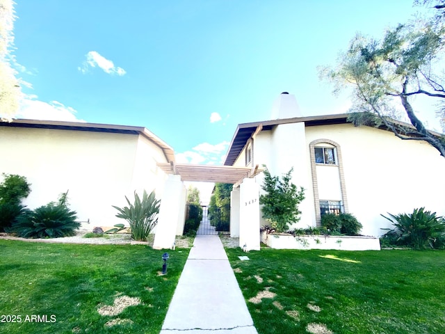 view of front of home featuring a front yard, a gate, a chimney, and stucco siding