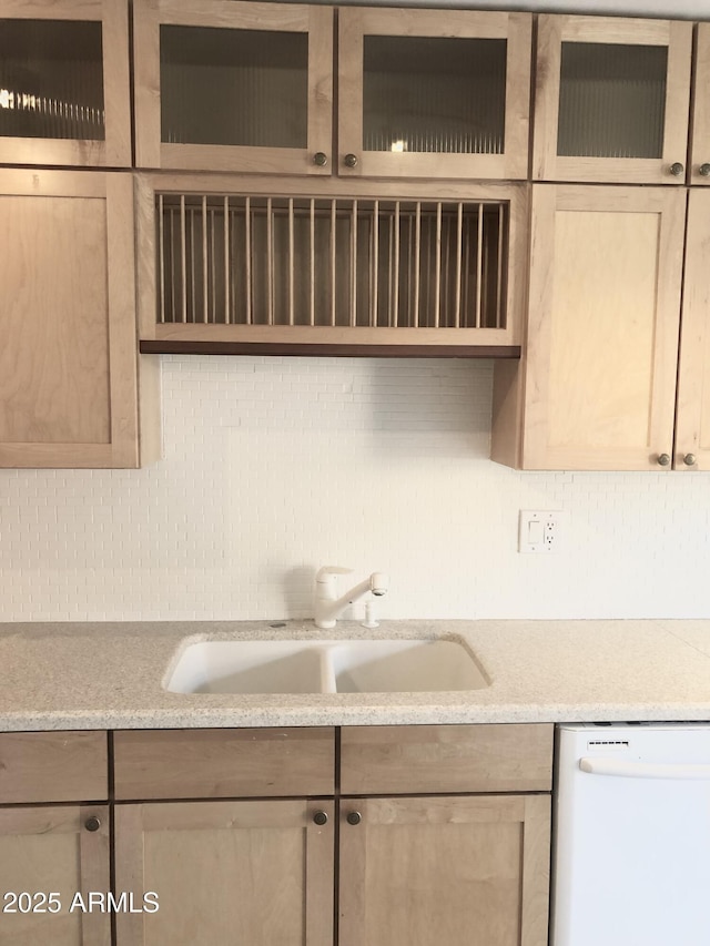 kitchen featuring white dishwasher, a sink, light countertops, decorative backsplash, and light brown cabinetry