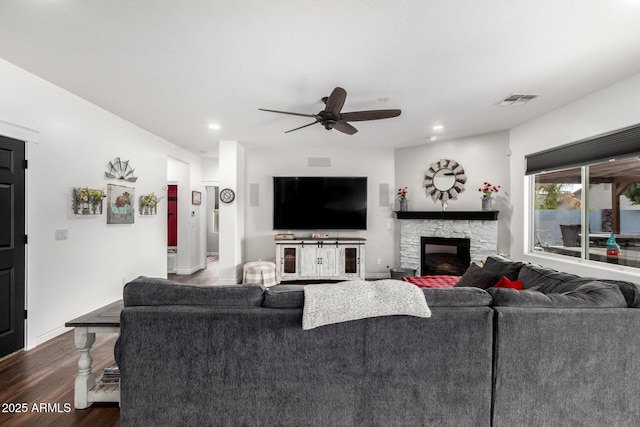 living room with ceiling fan, a fireplace, and dark wood-type flooring