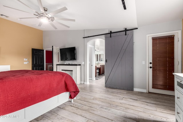 bedroom with ensuite bath, ceiling fan, a barn door, light hardwood / wood-style floors, and lofted ceiling