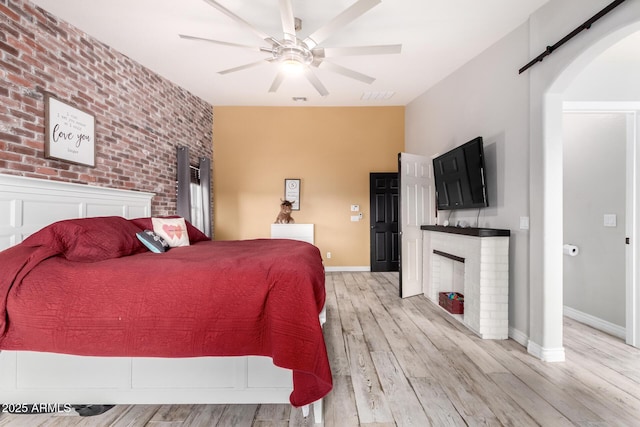 bedroom with ceiling fan, light hardwood / wood-style floors, a fireplace, and brick wall