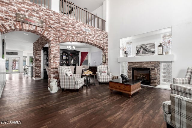 living room with a high ceiling, dark hardwood / wood-style flooring, an inviting chandelier, and a stone fireplace