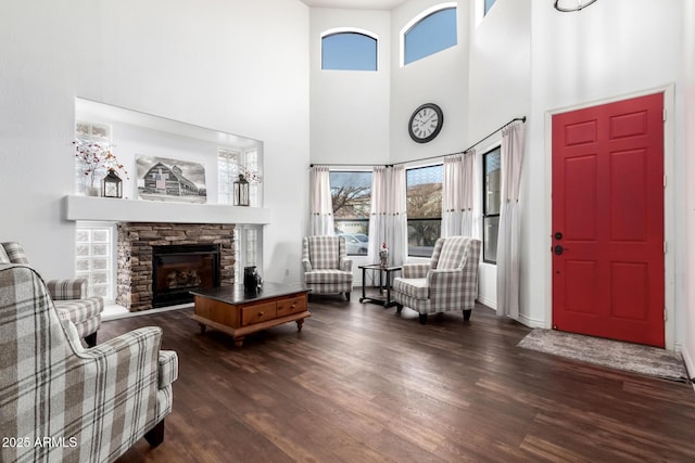 living room with a stone fireplace, dark hardwood / wood-style flooring, and a high ceiling