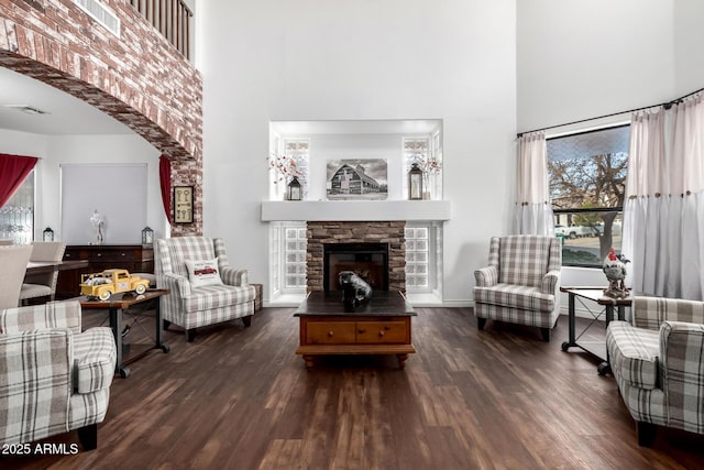 living room with a stone fireplace, dark wood-type flooring, and a high ceiling