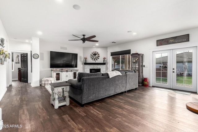 living room with a stone fireplace, ceiling fan, french doors, and dark hardwood / wood-style floors