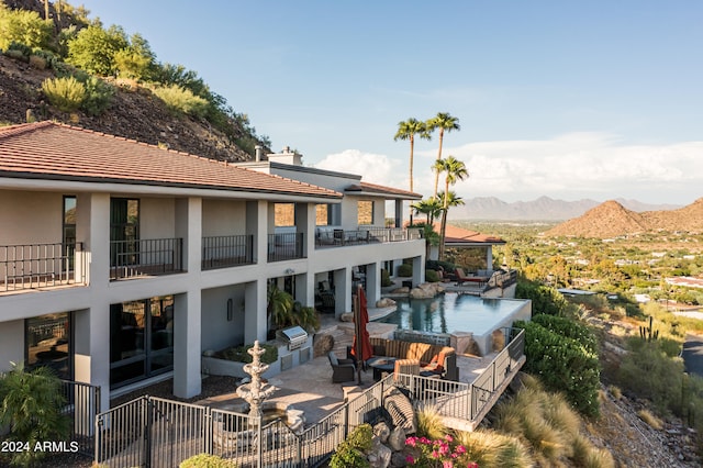 rear view of property featuring a mountain view, a balcony, a patio, and a fenced in pool