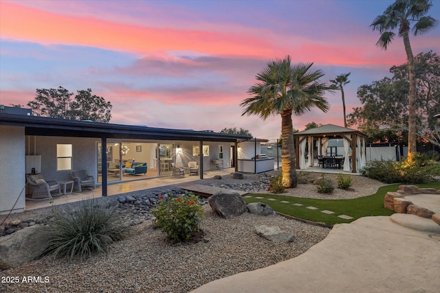 back of house at dusk featuring a patio area, fence, exterior kitchen, and a gazebo