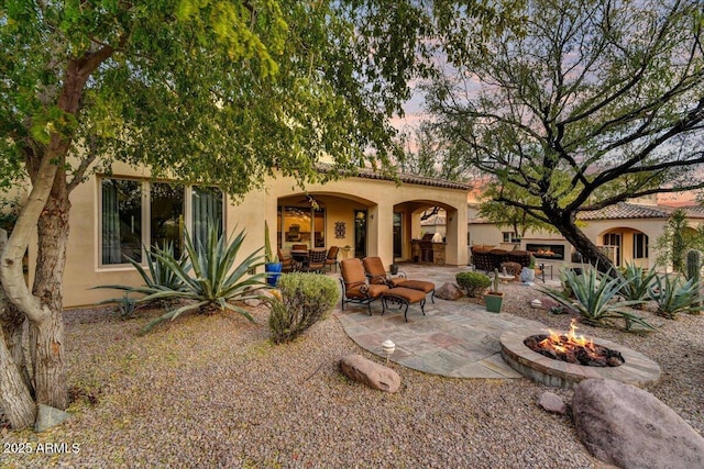2744 S First Water Ln, Gold Canyon, AZ 85118 - back of house featuring a tile roof, stucco siding, a warm lit fireplace, a fire pit, and a patio area