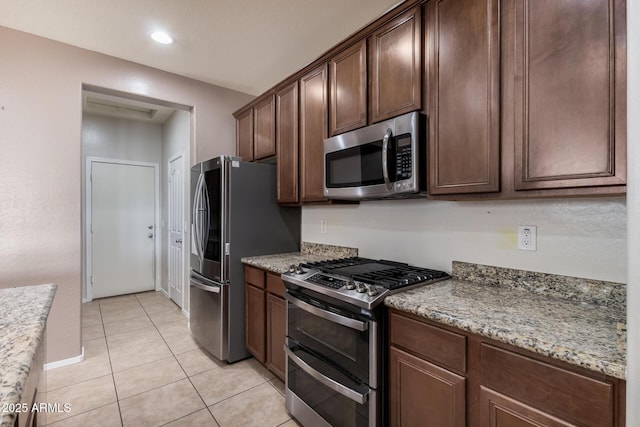 kitchen featuring light stone countertops, appliances with stainless steel finishes, dark brown cabinets, and light tile patterned flooring