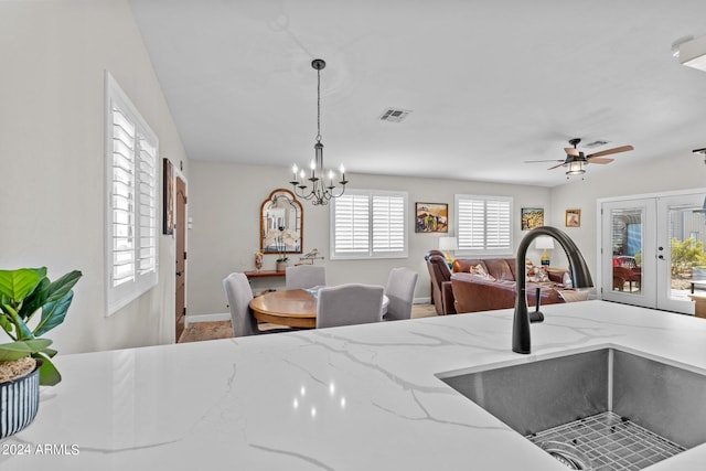 kitchen with french doors, light stone counters, ceiling fan with notable chandelier, sink, and decorative light fixtures