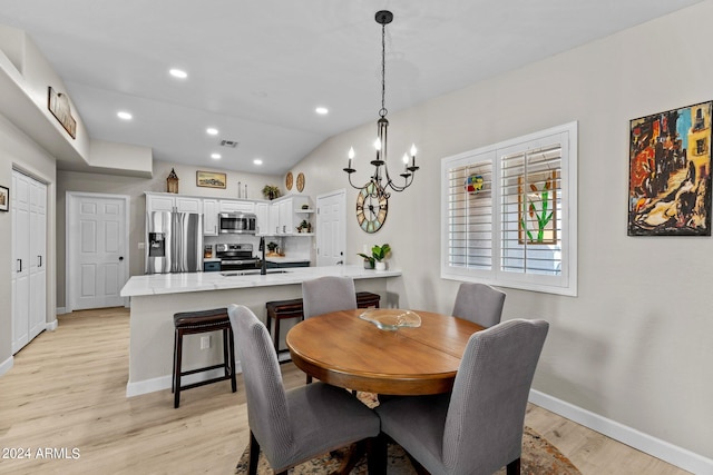 dining space with lofted ceiling, light wood-type flooring, sink, and a chandelier