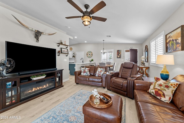 living room with plenty of natural light, light wood-type flooring, ceiling fan with notable chandelier, and vaulted ceiling